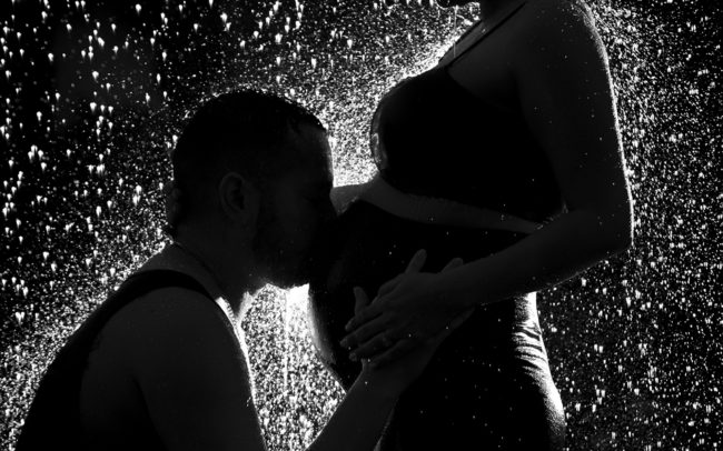 Maternity couple silhouette kissing belly in the rain